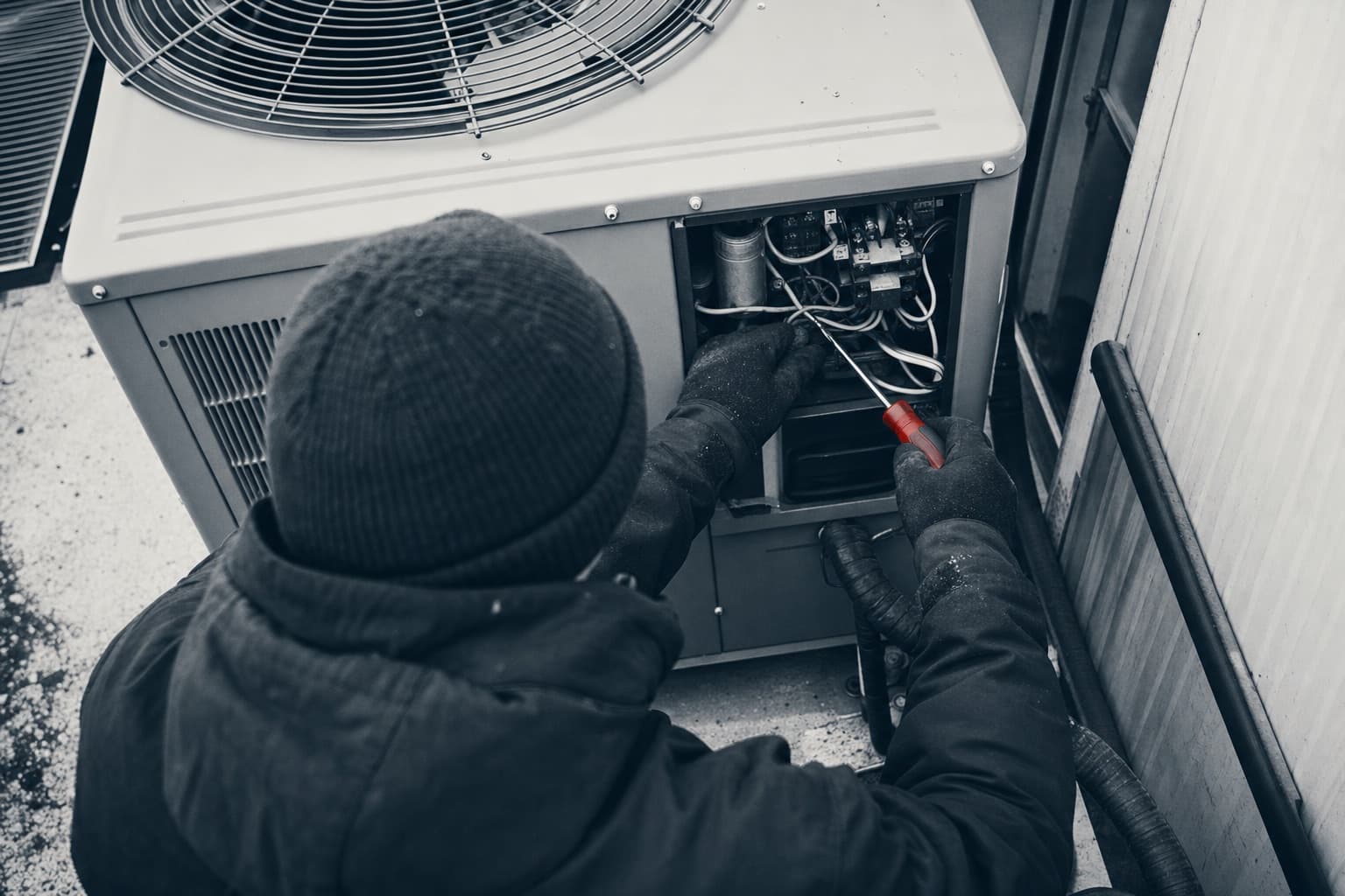 Gloved hands of an HVAC technician servicing an open outdoor condenser unit with a red-handled screwdriver